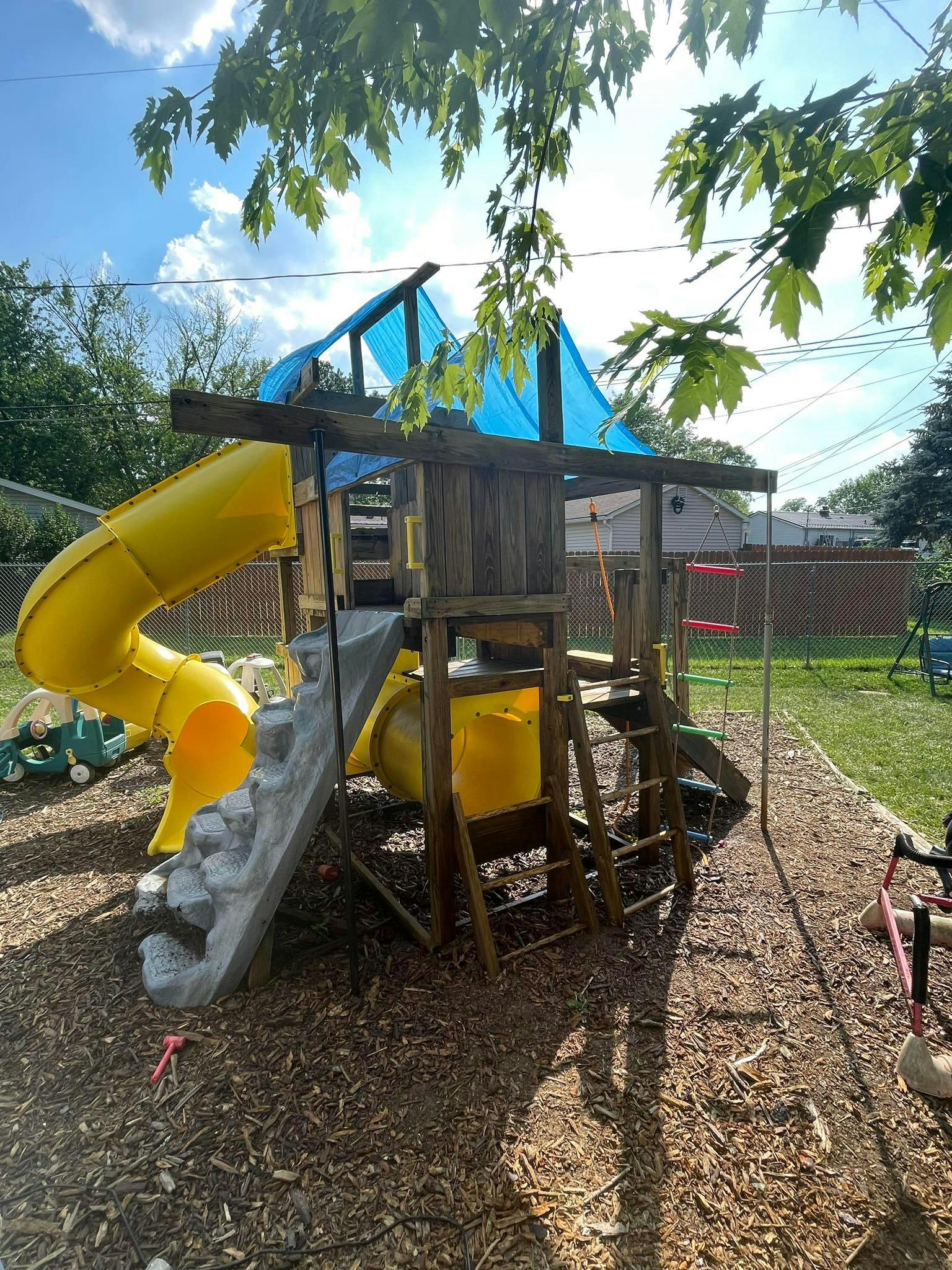 Wooden playground set with yellow slides and blue tarp roof