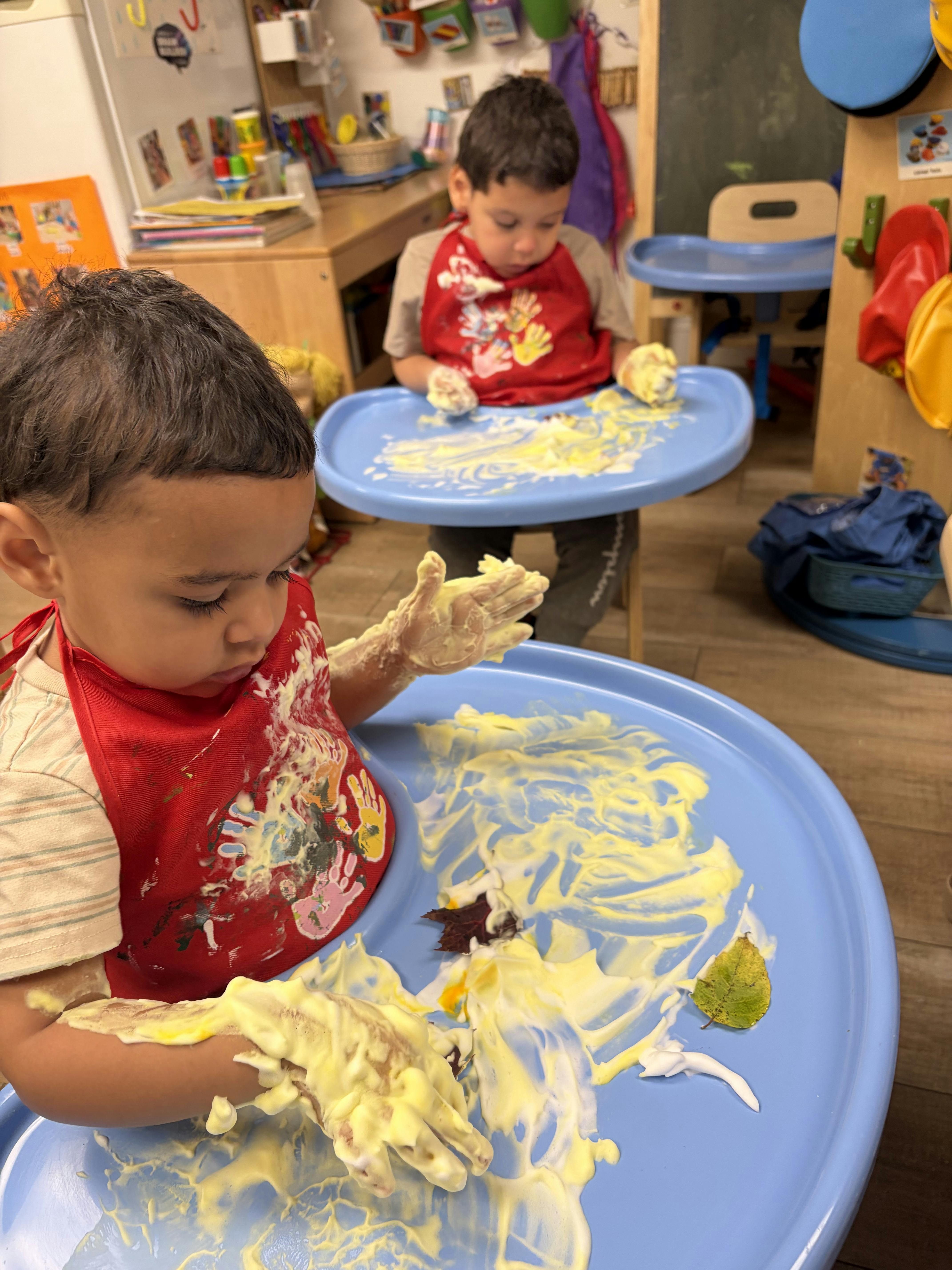 Children wearing red aprons playing with yellow paint on plastic trays