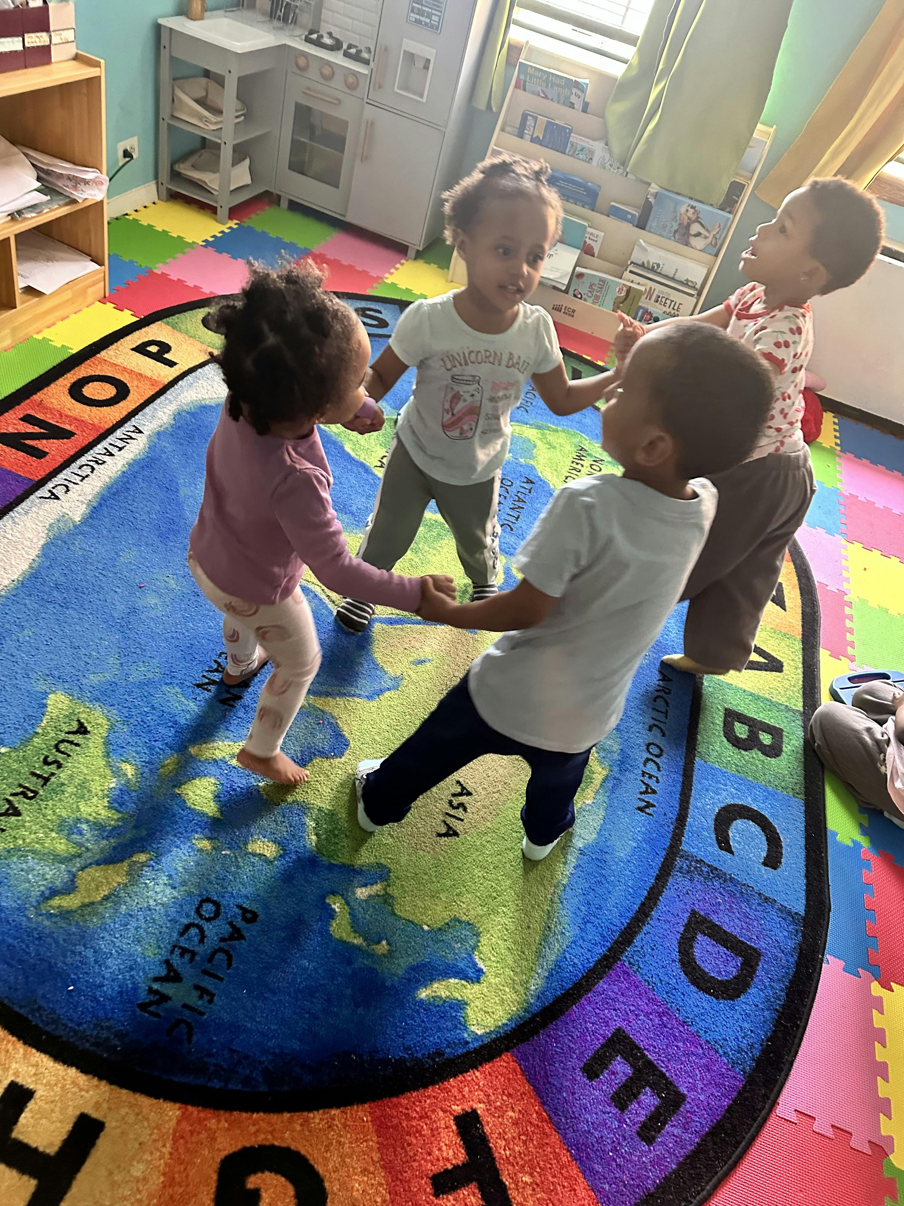 Four children holding hands and walking in a circle on a map rug