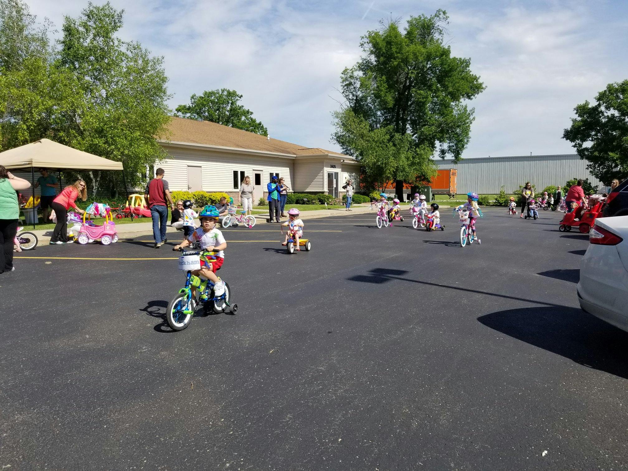 Children riding bikes and tricycles in a parking lot
