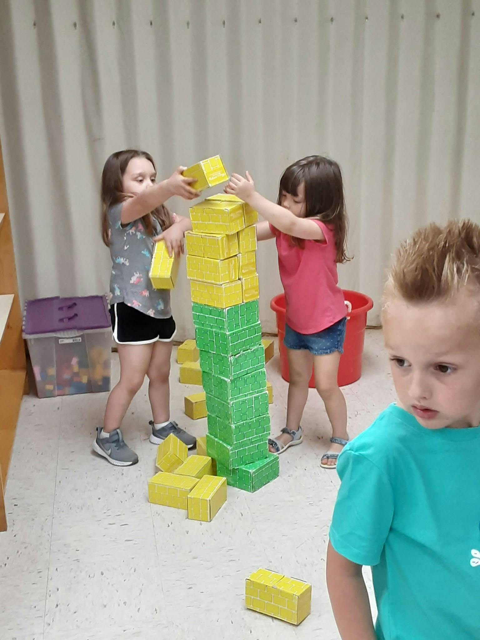Two children building a tall tower with yellow and green blocks