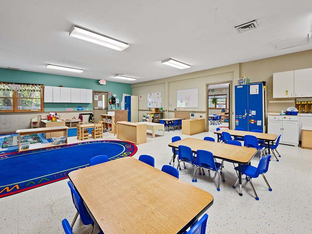 Classroom with small tables, blue chairs, and a blue rug