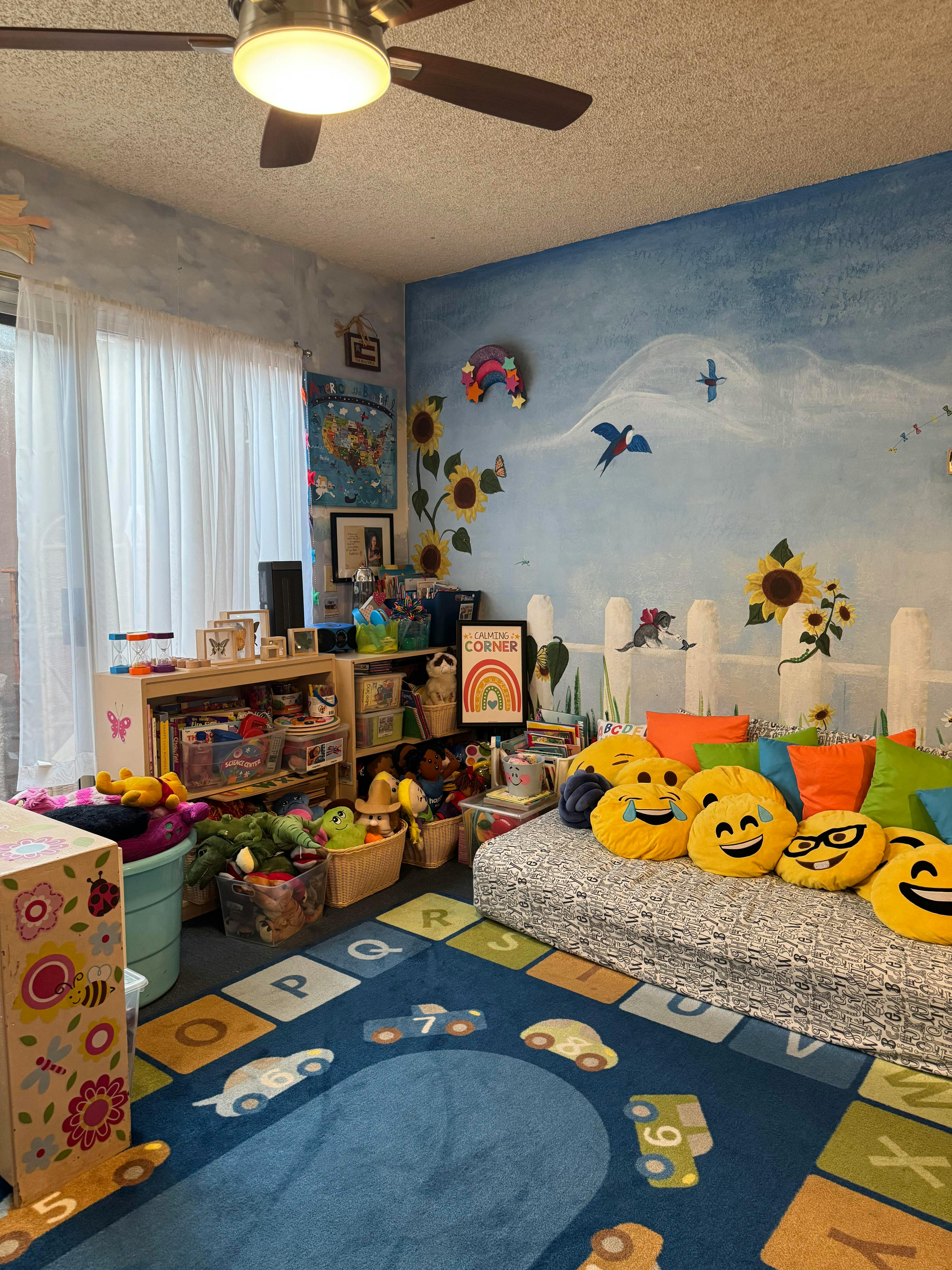 Playroom with a blue rug, shelves of toys, and a bed with emoji pillows