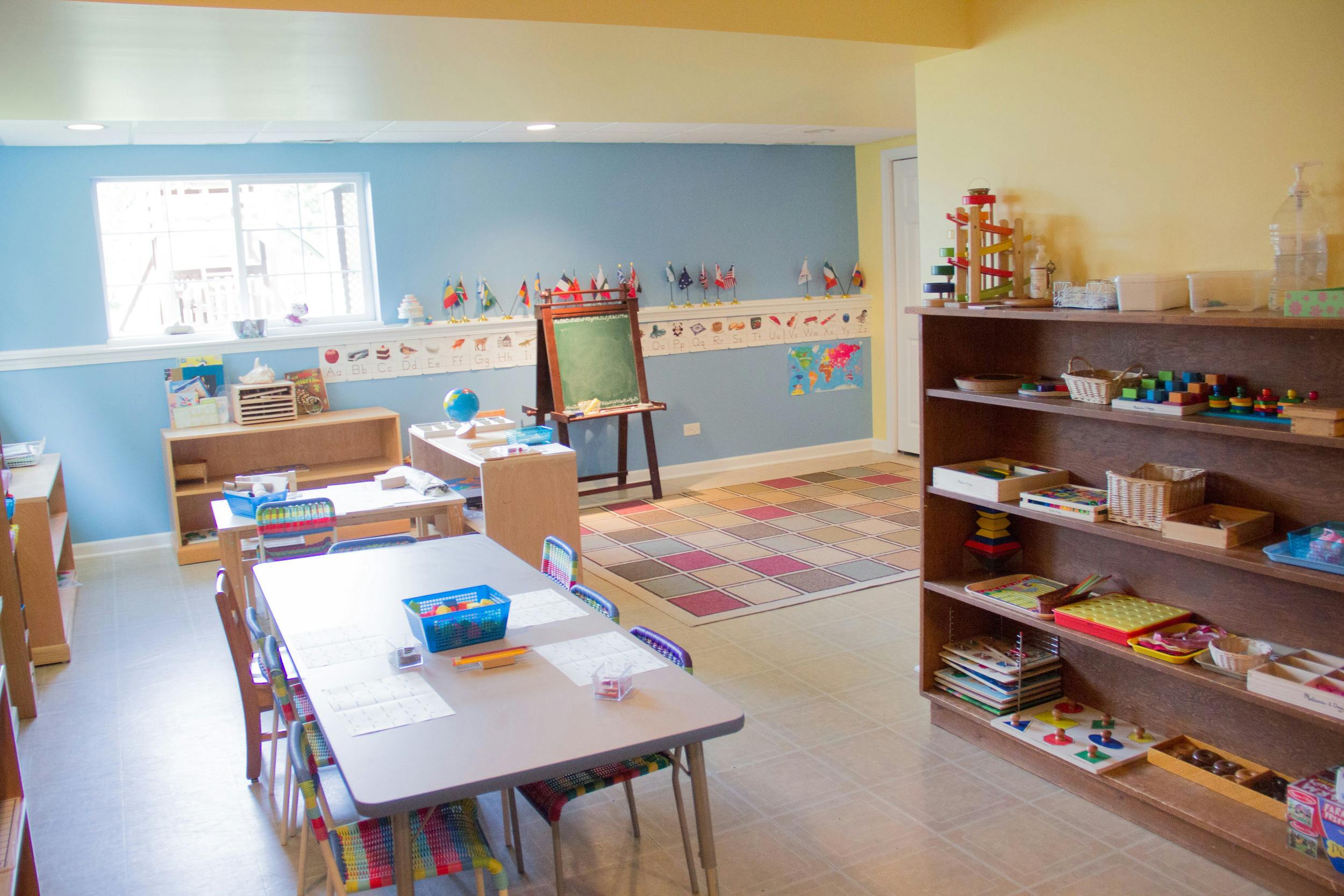 Classroom with tables, chairs, shelves, and a chalkboard