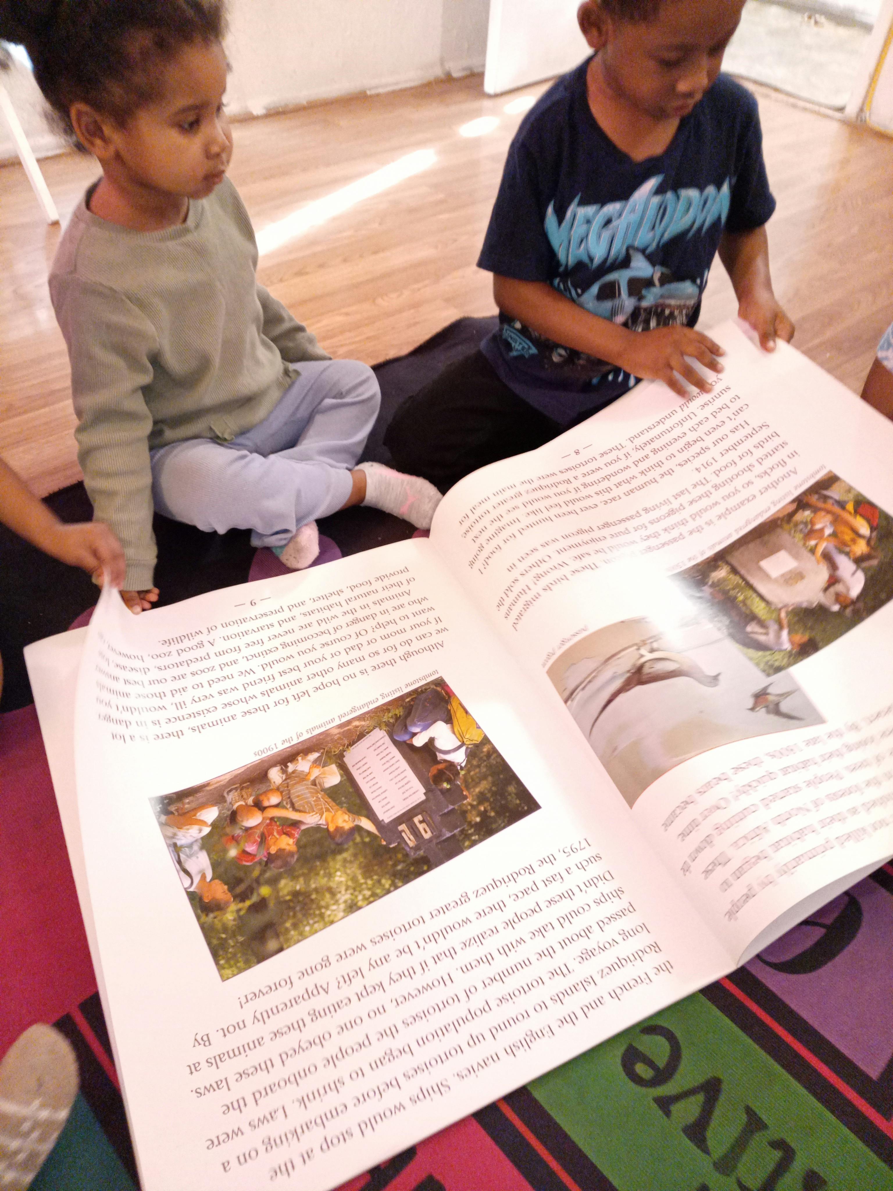 two children on the floor looking at a large open book