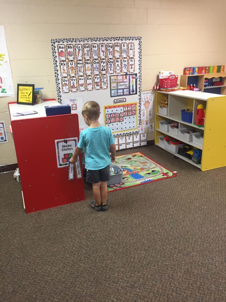 Child standing in front of a red book station in a classroom