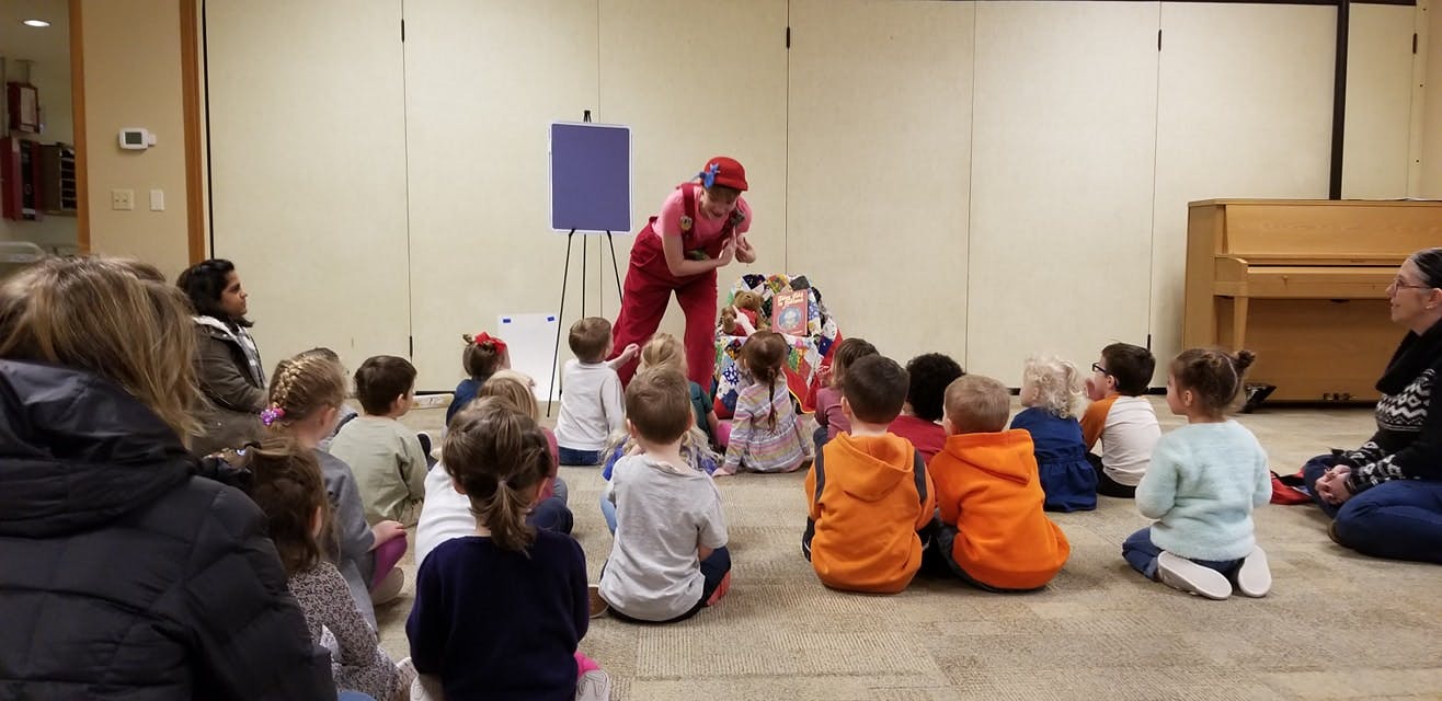 Person in red costume performing for children sitting on the floor