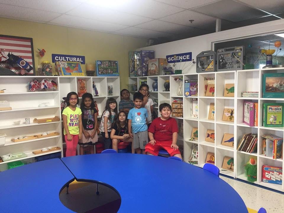 Group of children standing in a classroom with shelves of books and learning materials