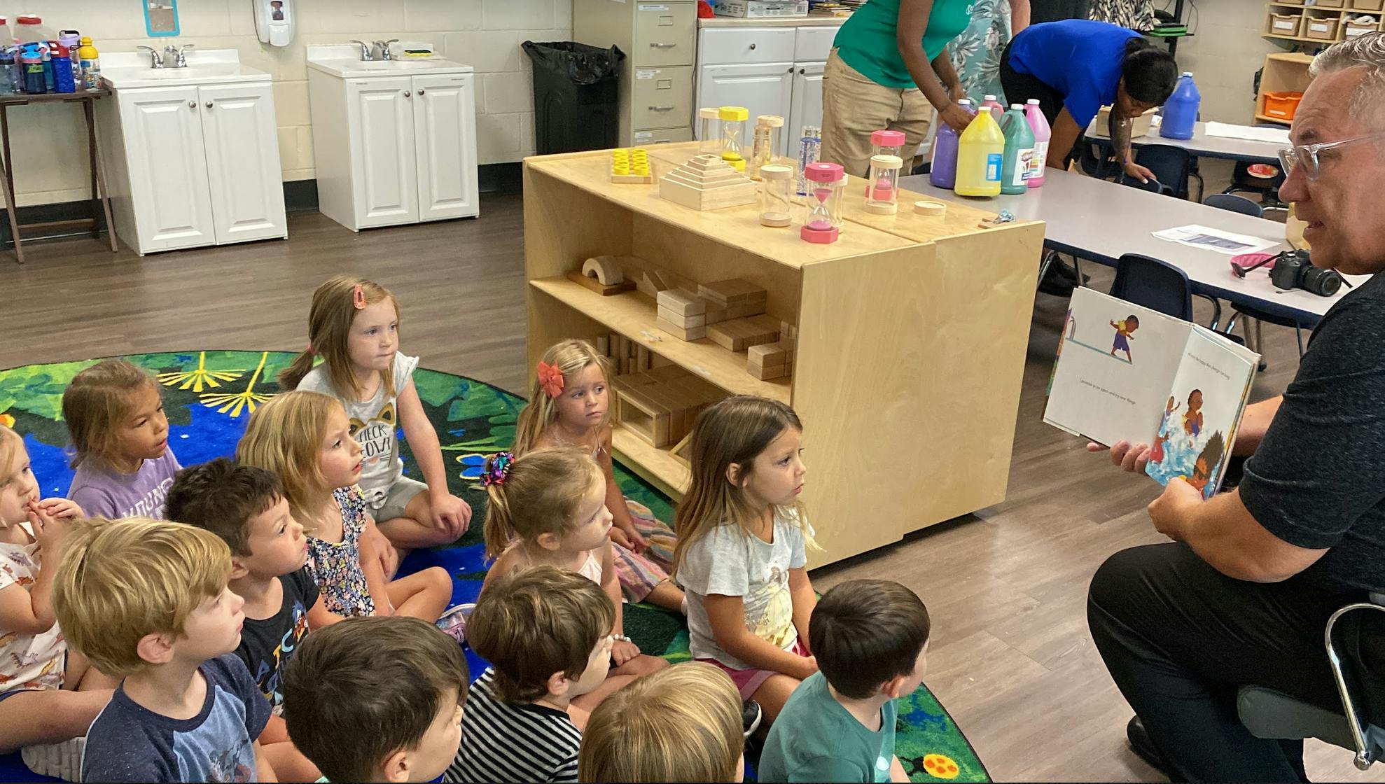 Adult reading a book to a group of children in a classroom