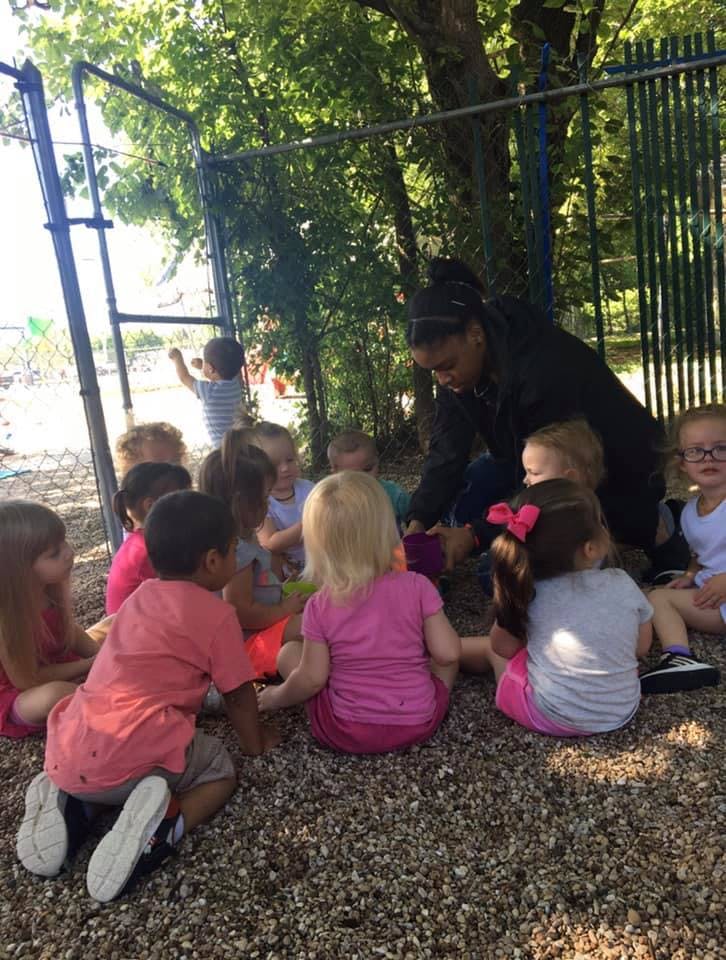 Adult and children sitting on the ground outdoors