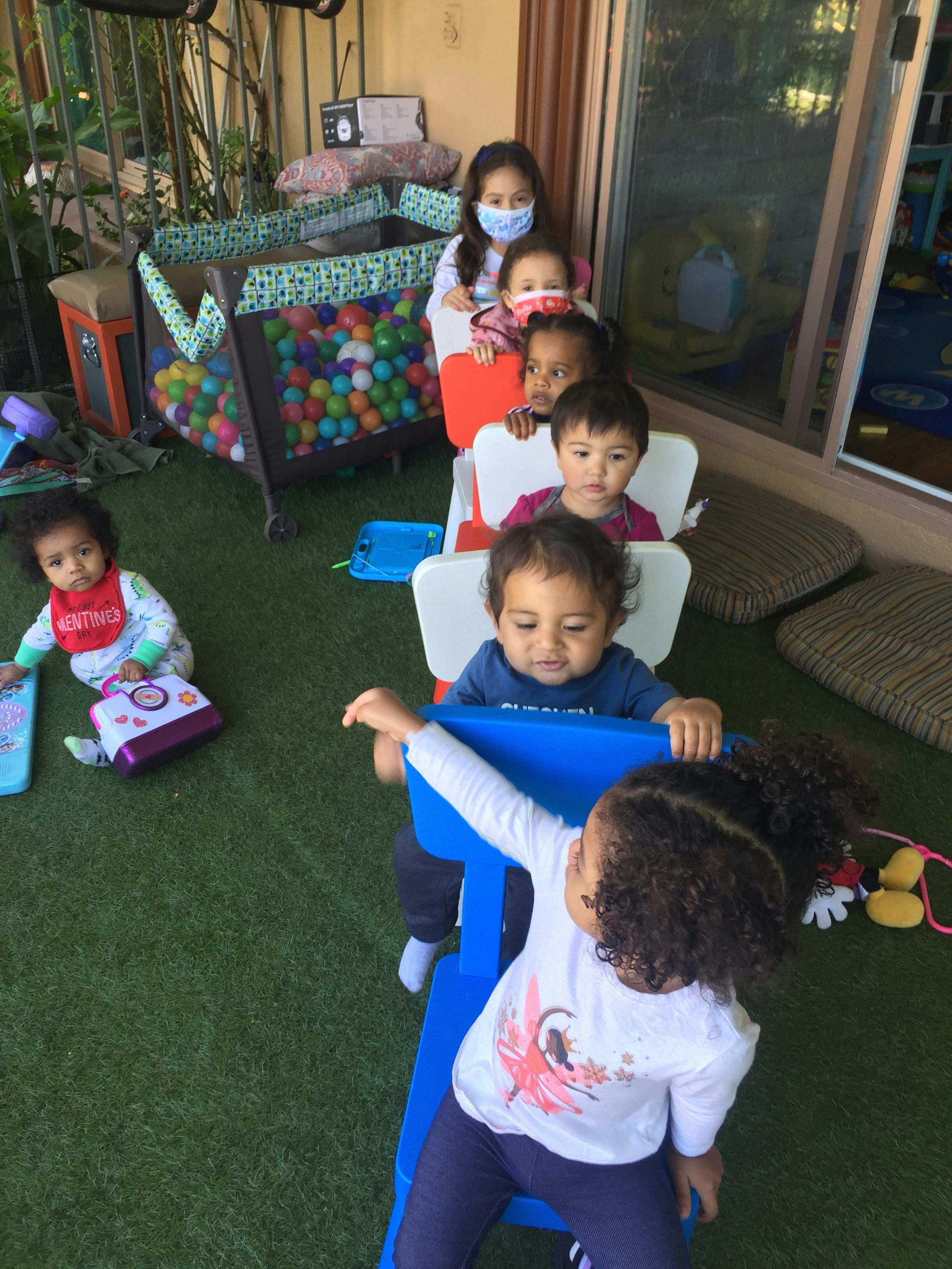 Children sitting in a line of chairs, one child on the ground