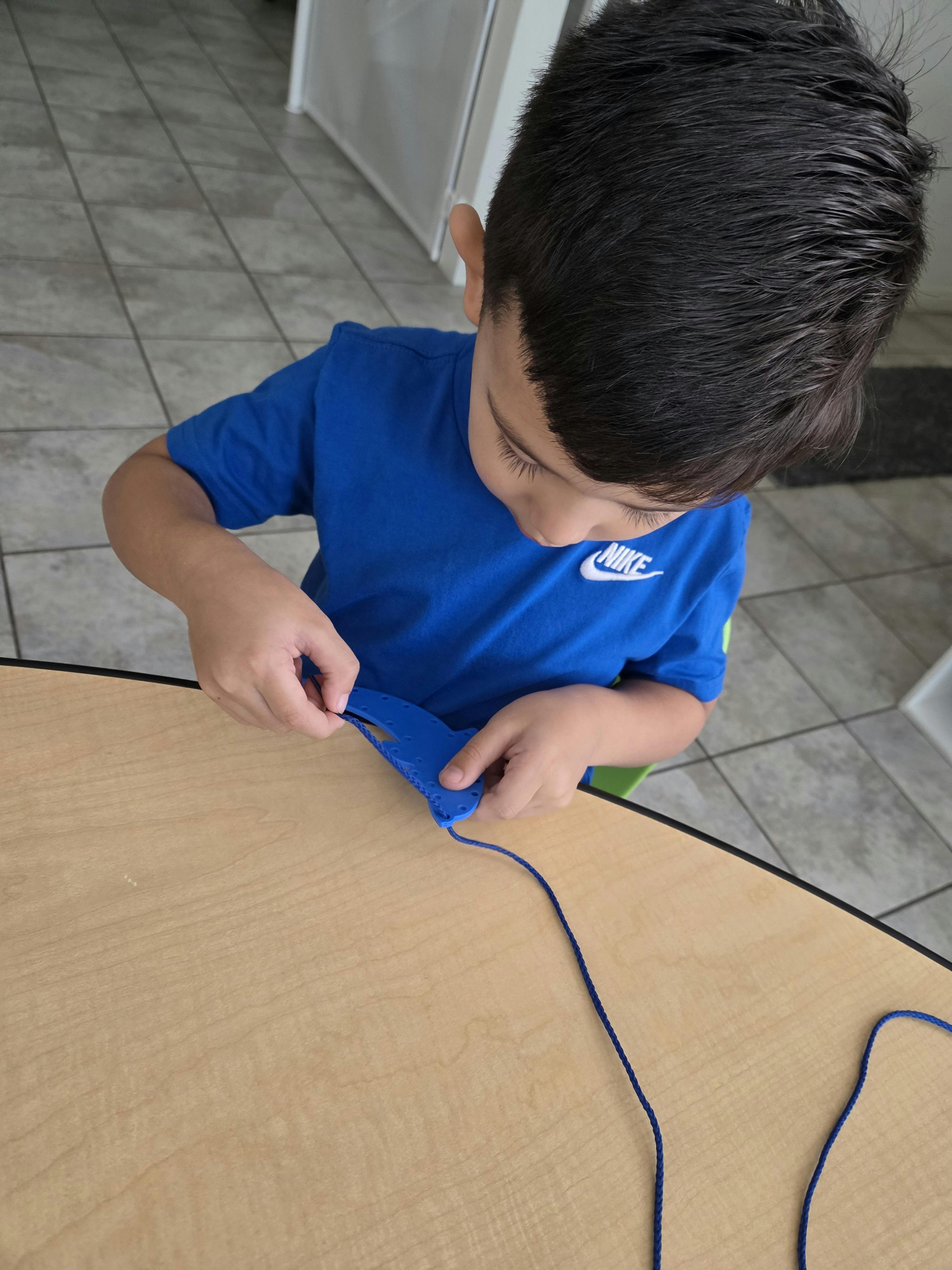 Child threading a string through a plastic craft shape at a table