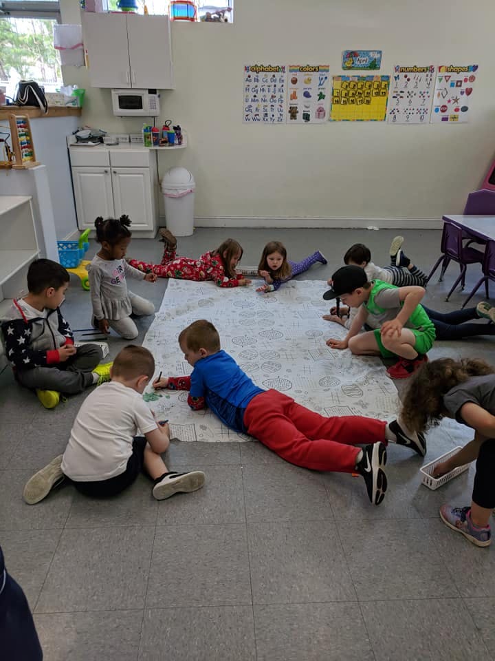Children on the floor in a classroom, some drawing on a large sheet