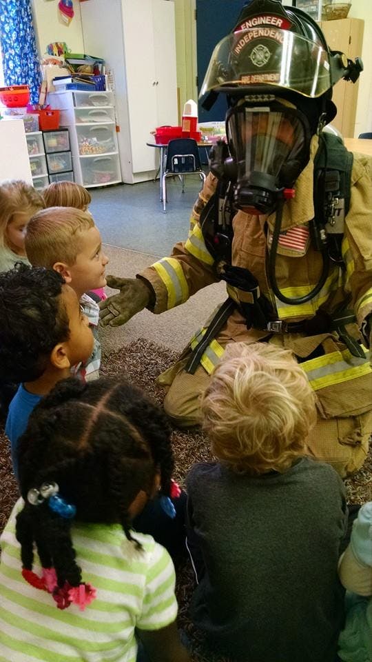 Person in firefighter gear kneeling with children in a classroom