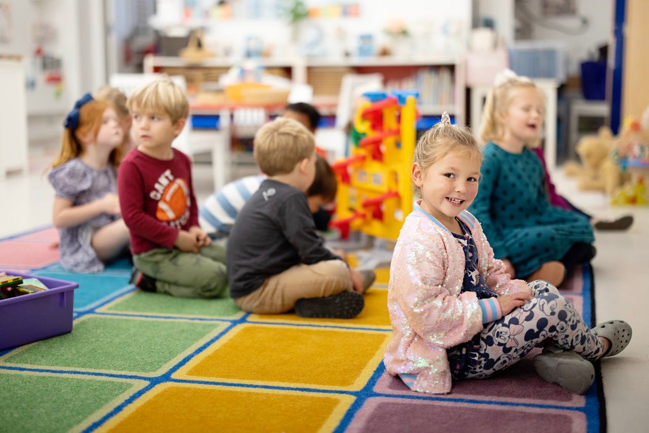 Children sitting on a colorful rug in a classroom