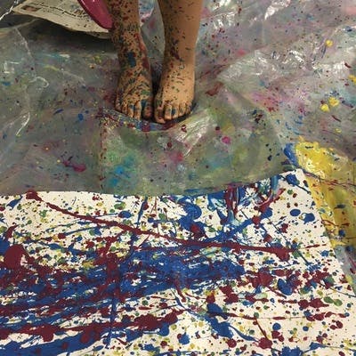 Child's paint-splattered feet standing on a paint-splattered tarp