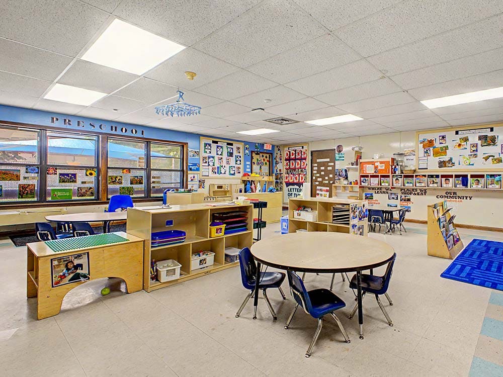 Empty preschool classroom with small tables, chairs, and learning materials