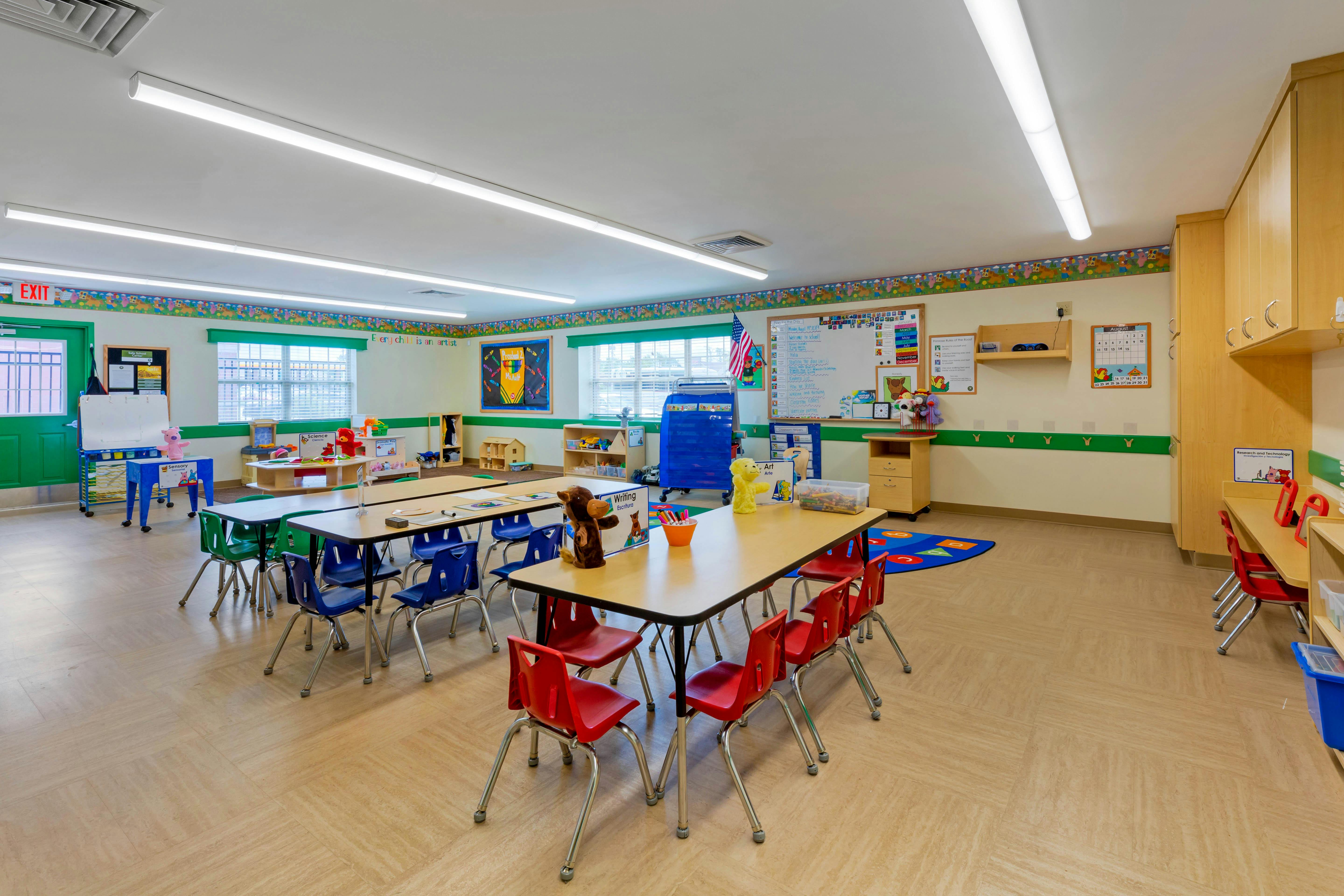 Empty classroom with small tables and chairs, whiteboard, and colorful decorations