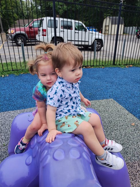 Two children sitting on a purple playground toy