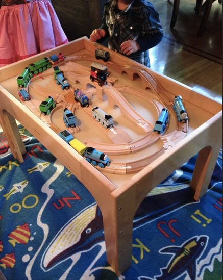 Child playing with toy trains on a wooden train table