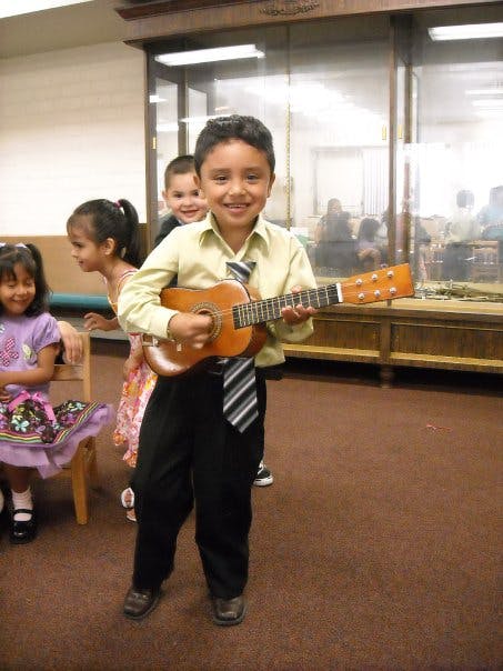 Child in a tie holding a small guitar