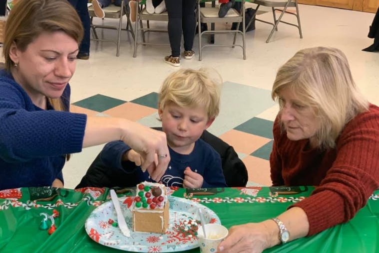 Two people and a child decorating a gingerbread house