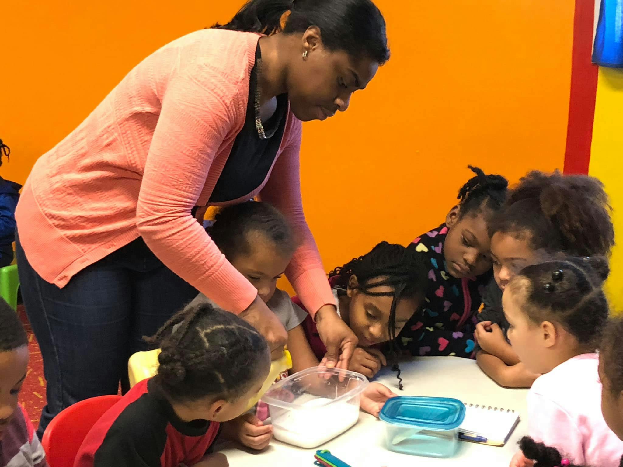 Adult and children gathered around a table looking at a container