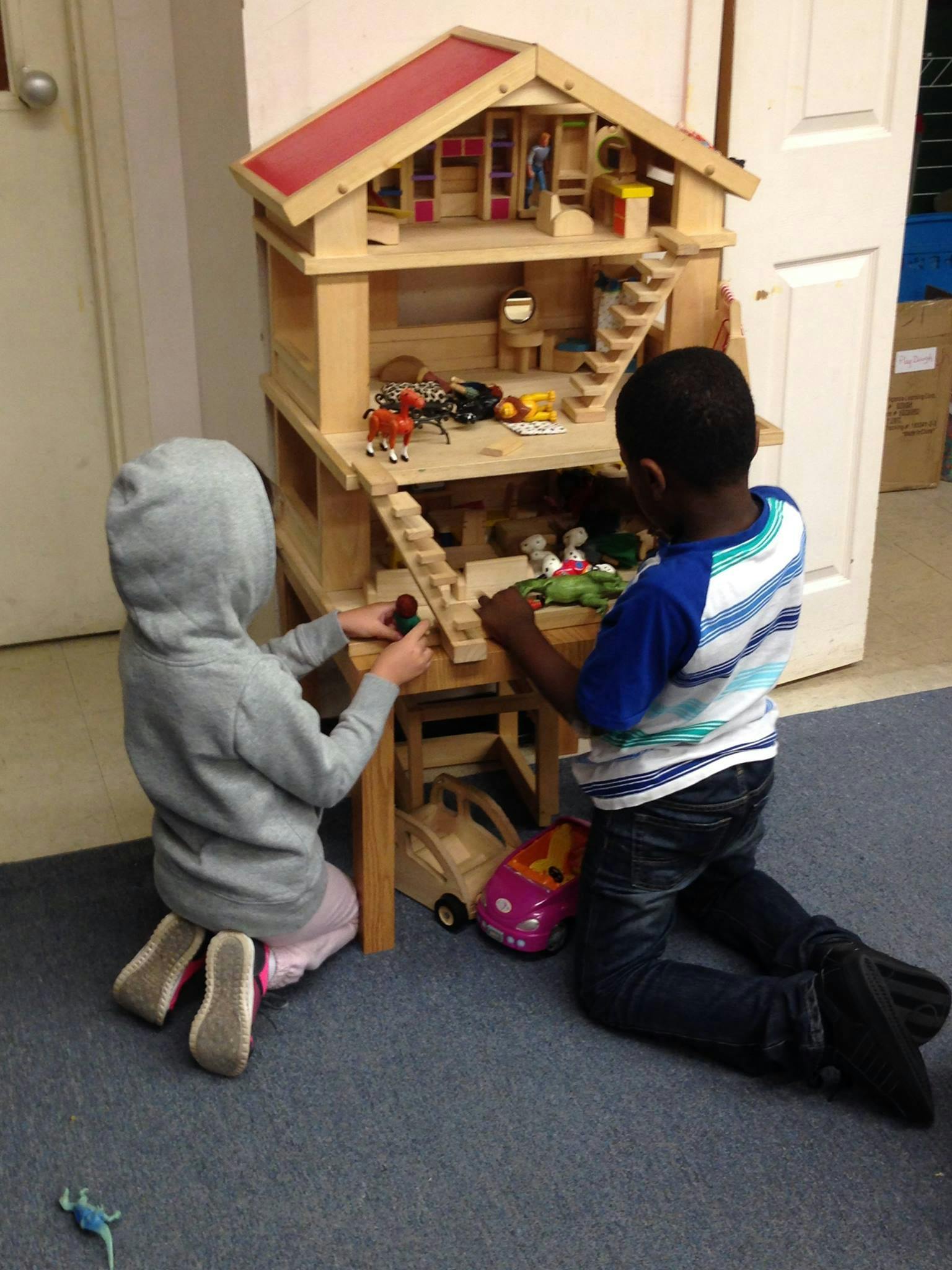 Two children playing with a wooden dollhouse