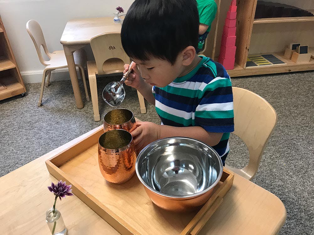 Child using a ladle to pour liquid into cups in a classroom