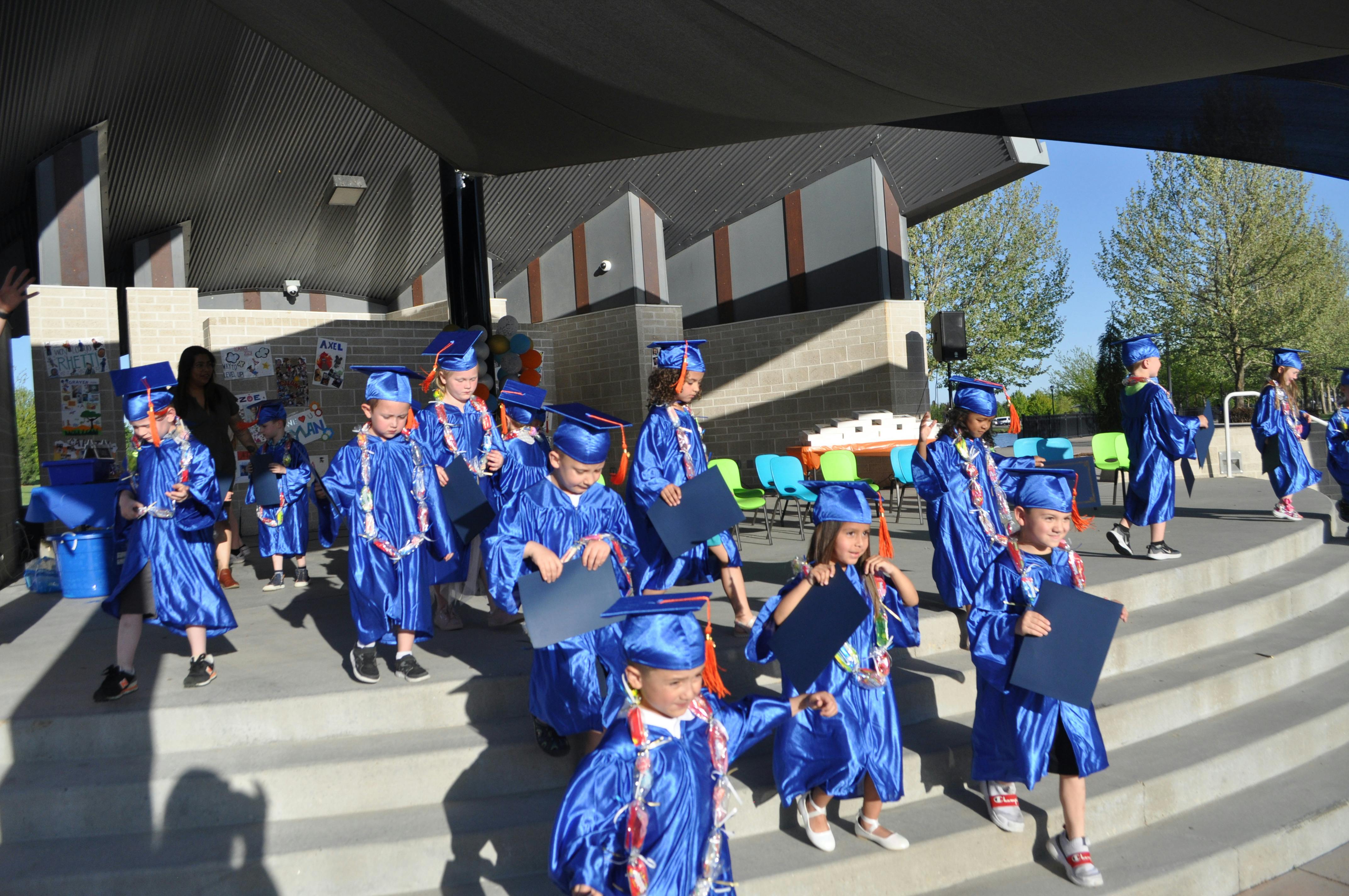 Children in blue graduation caps and gowns walking down steps