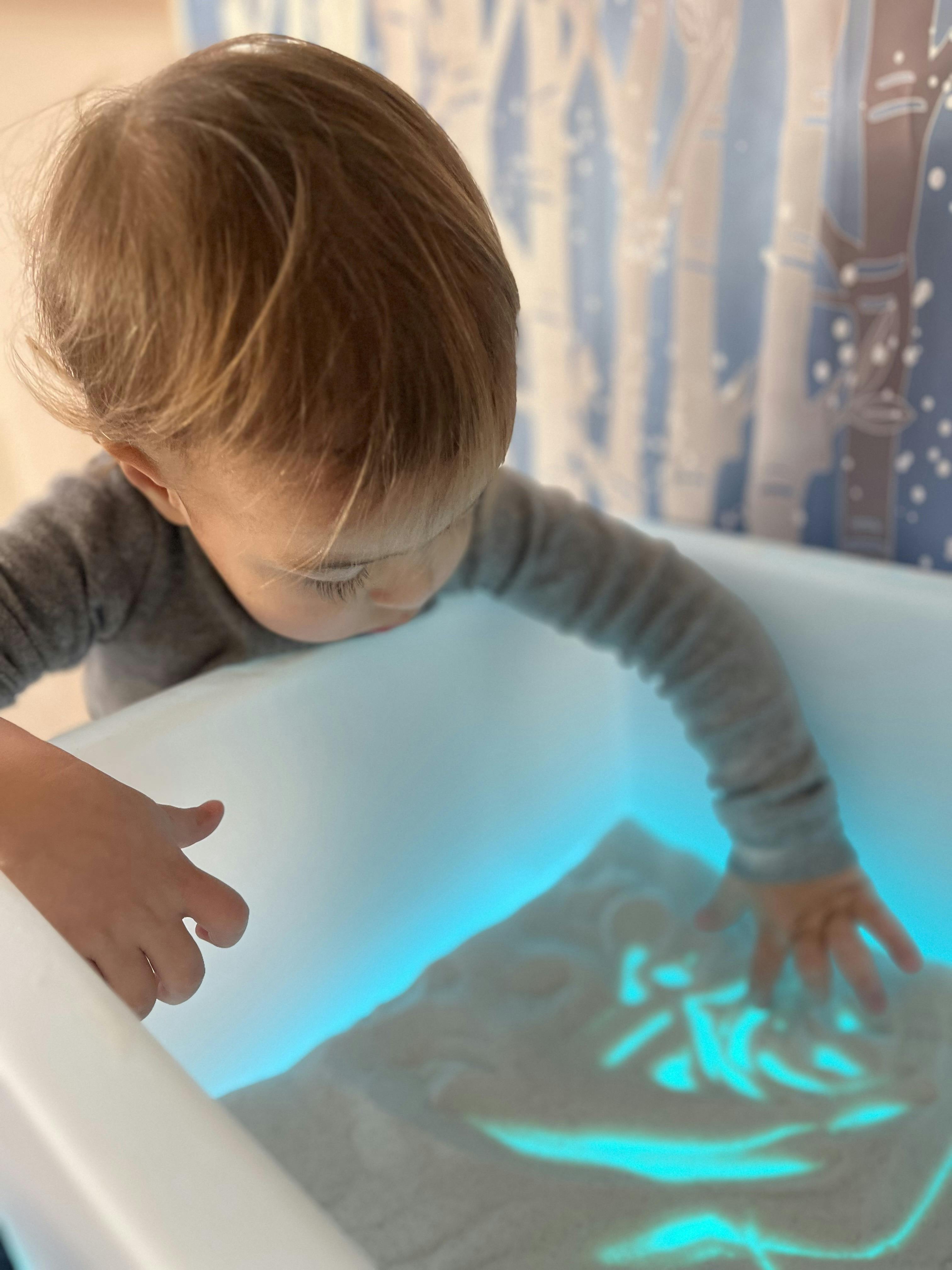 Child playing with sand in an illuminated sensory light table