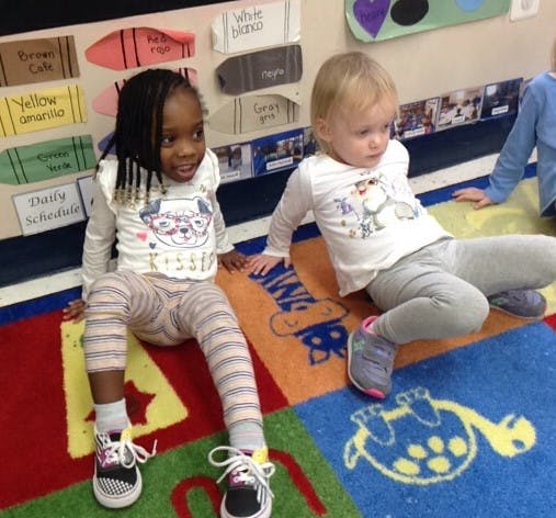 Two children sitting on a colorful rug in a classroom