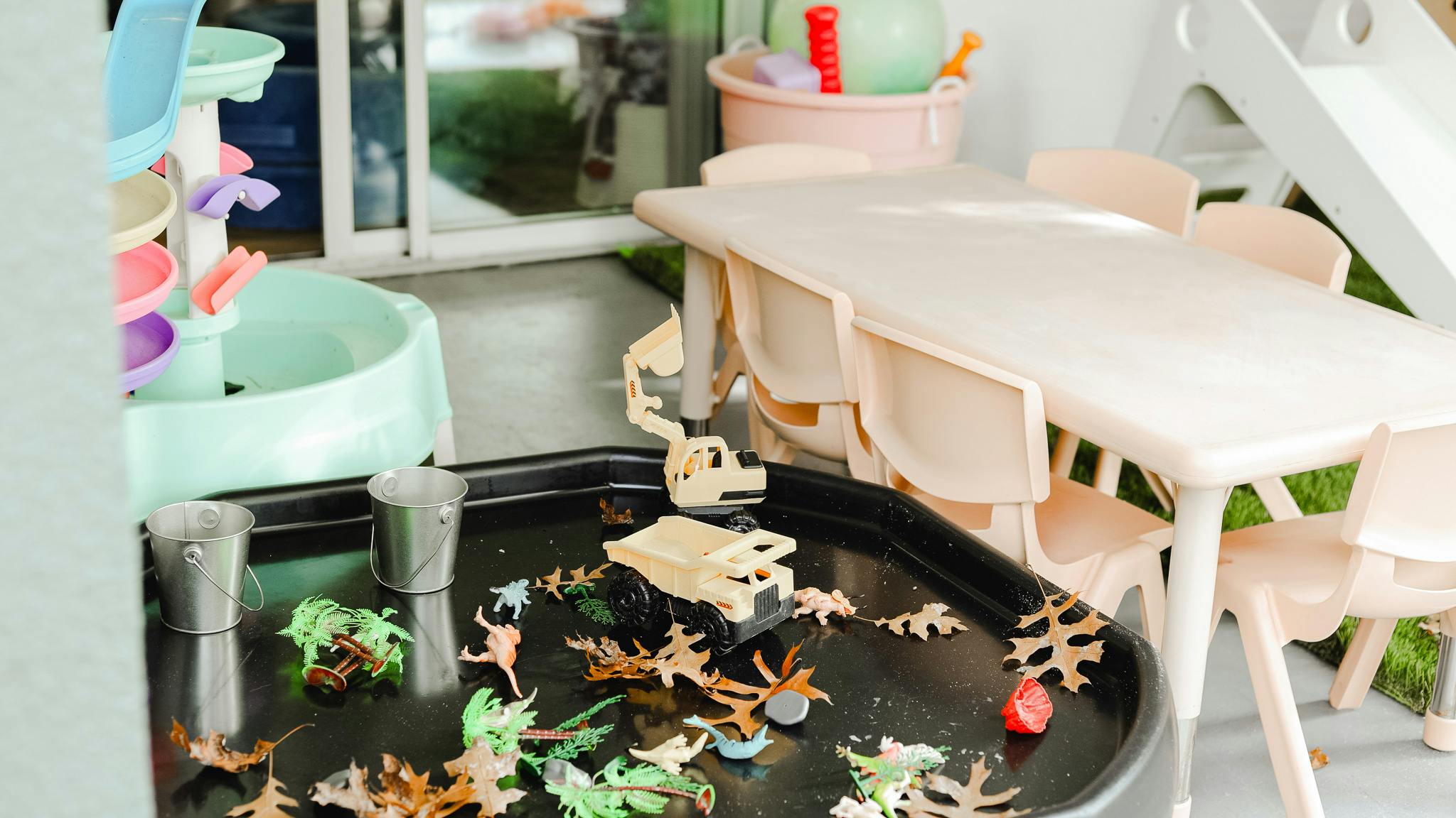 Play area with water table, small table and chairs, and toy animals in a tray