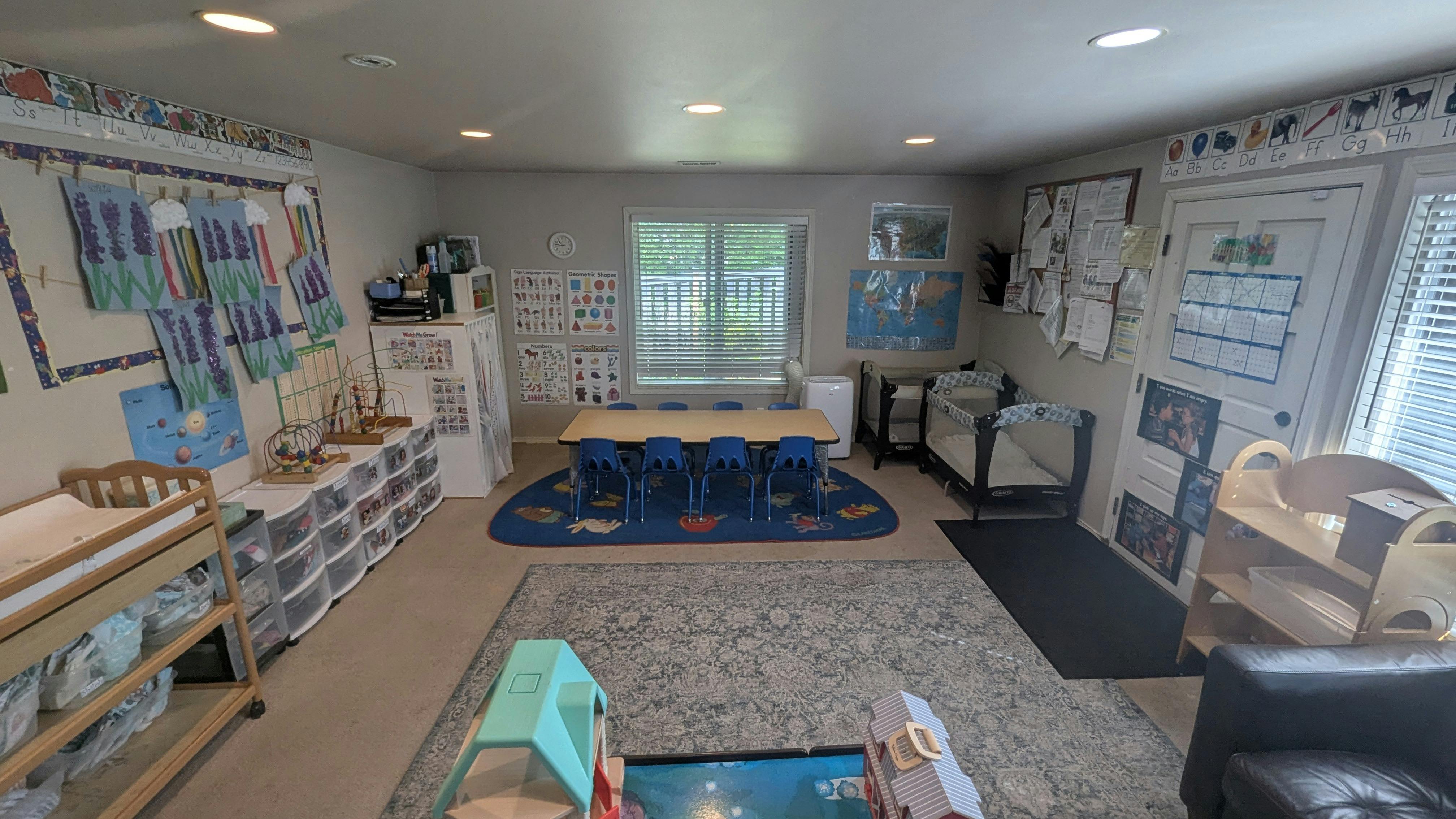 A classroom with small tables and chairs, educational posters on walls, and cribs