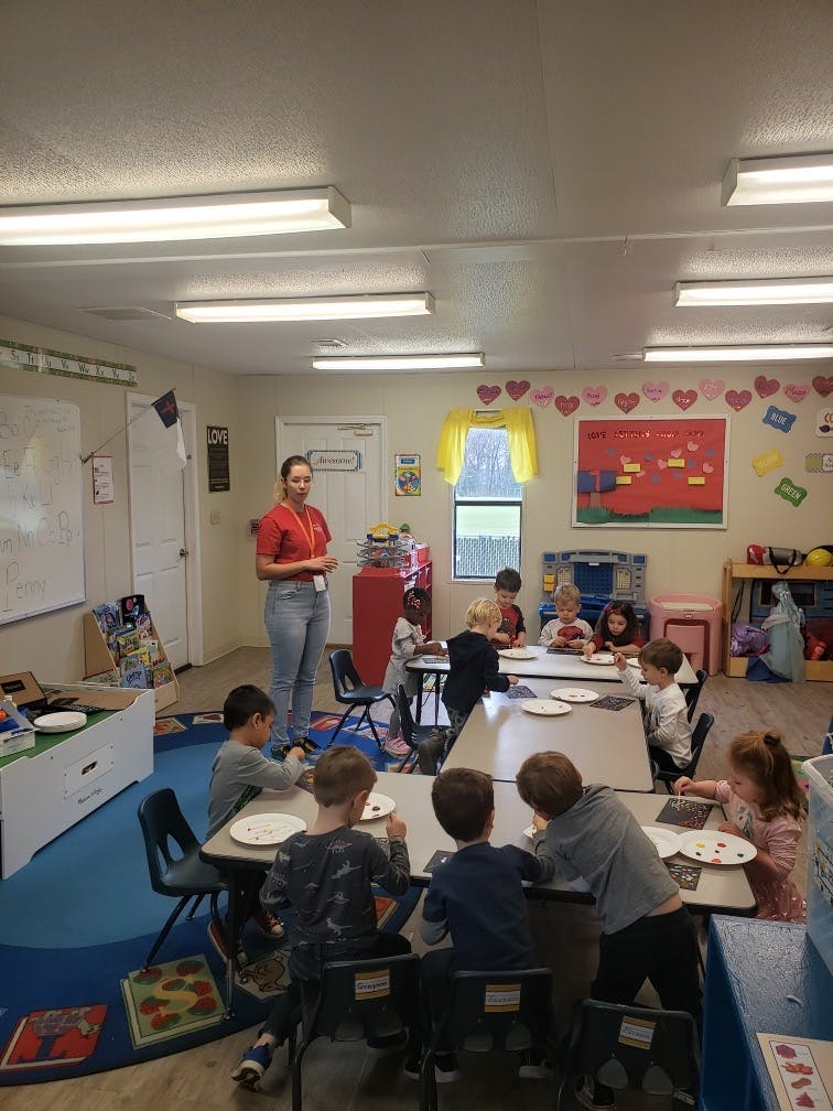 Adult standing in a classroom with children seated at tables