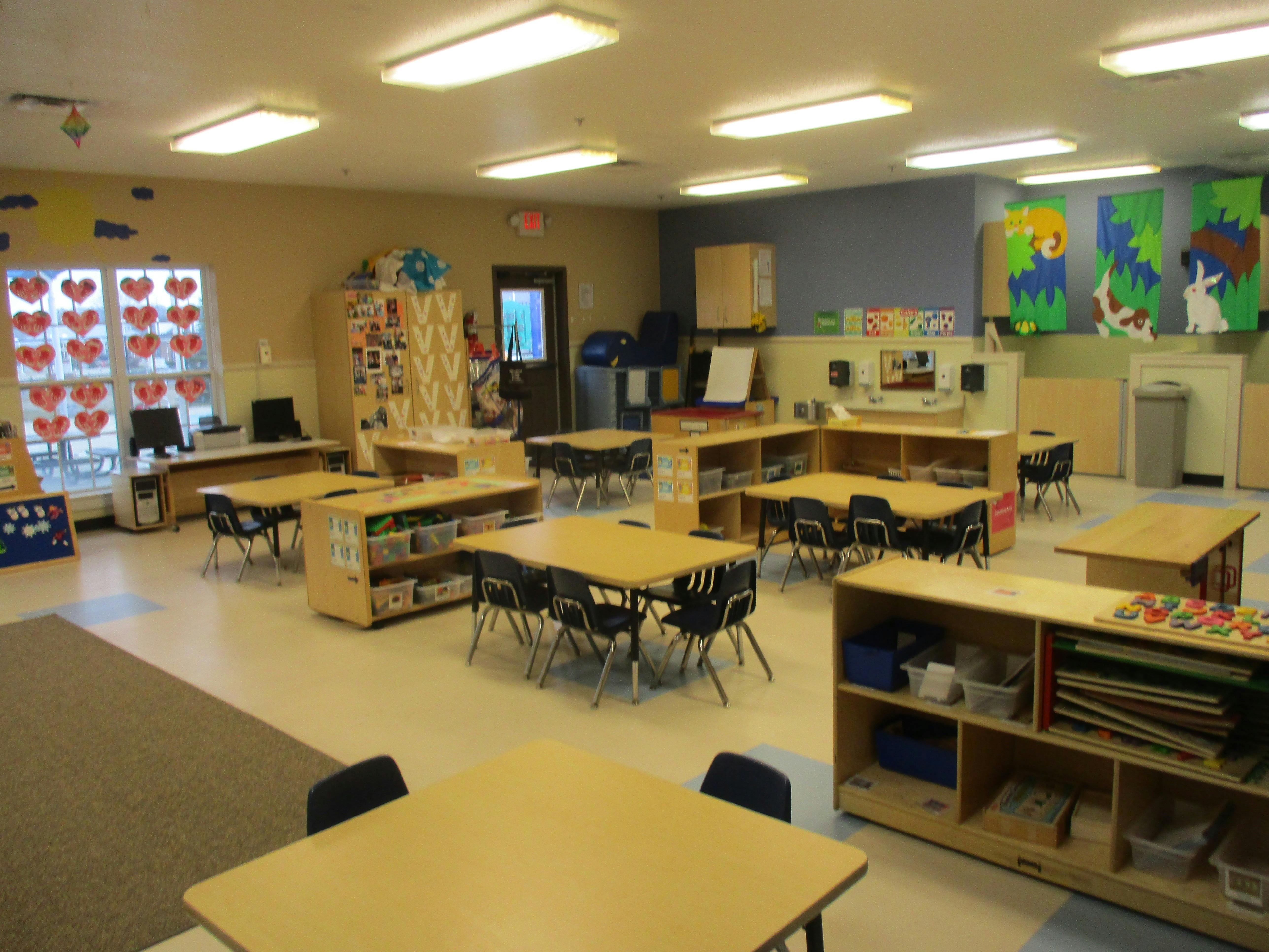 Empty classroom with tables and chairs, shelves of toys and books