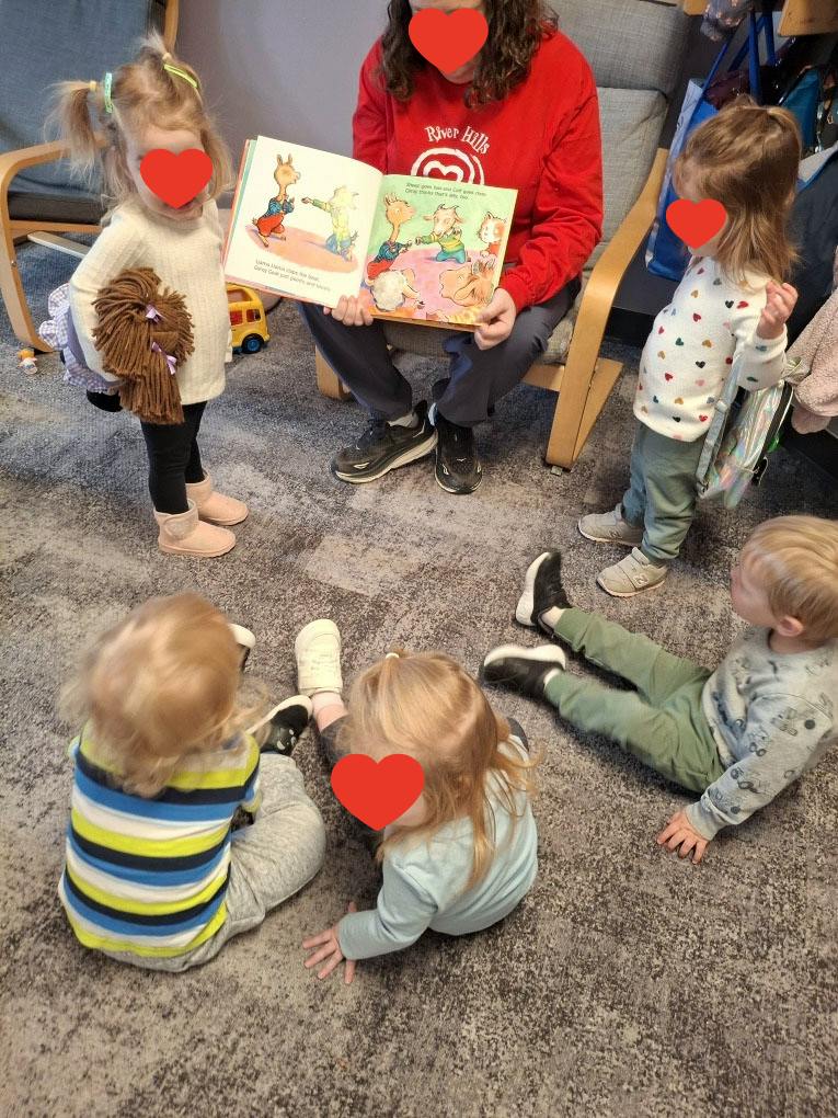 Adult reading a picture book to a group of children sitting on the floor