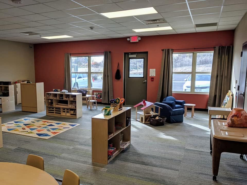 Classroom with small tables, chairs, and shelves with a colorful rug