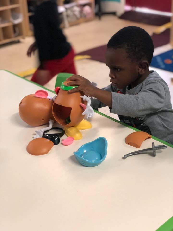 Child playing with a Mr. Potato Head toy on a table