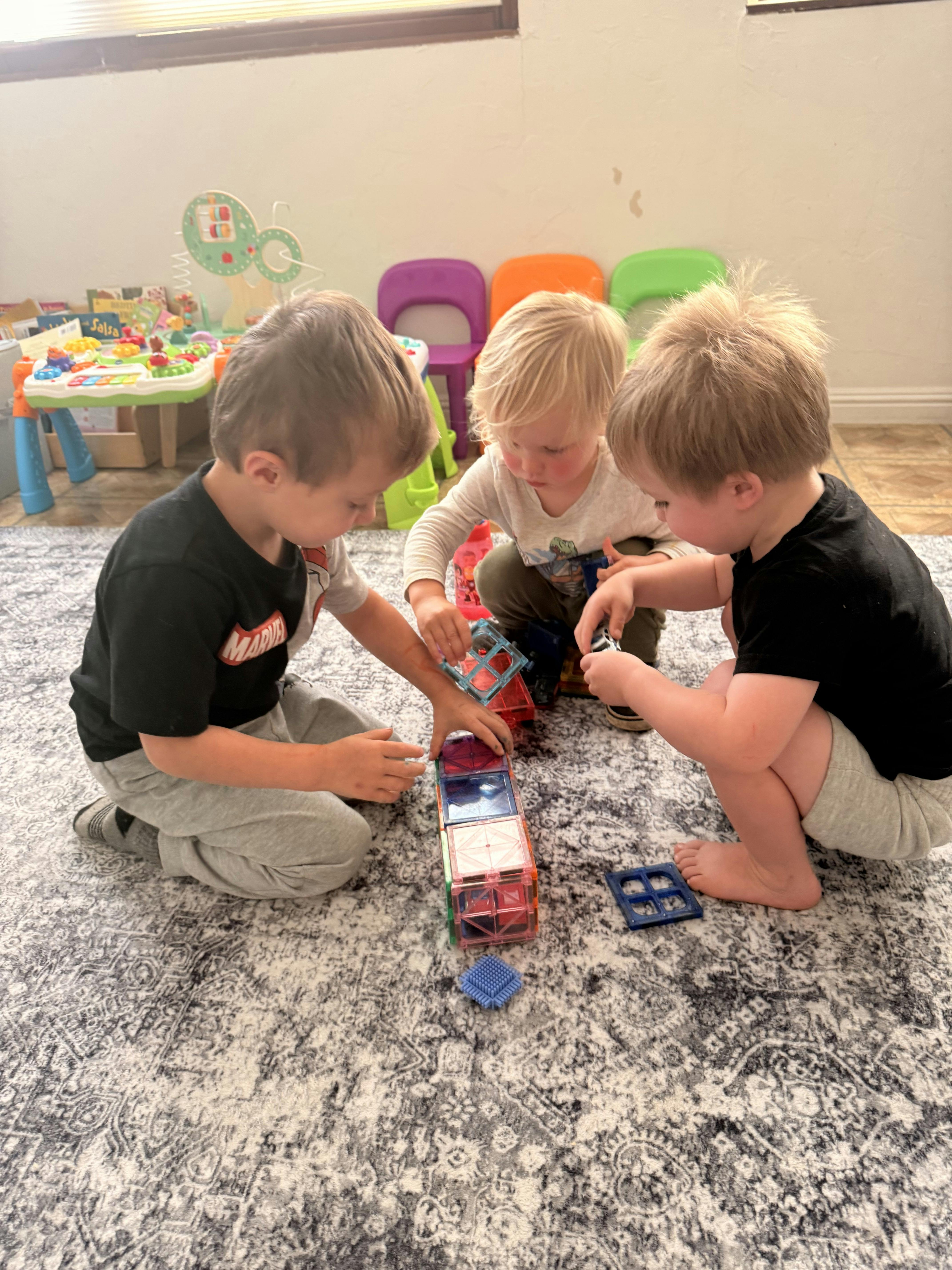 Three children playing with magnetic building tiles on a rug