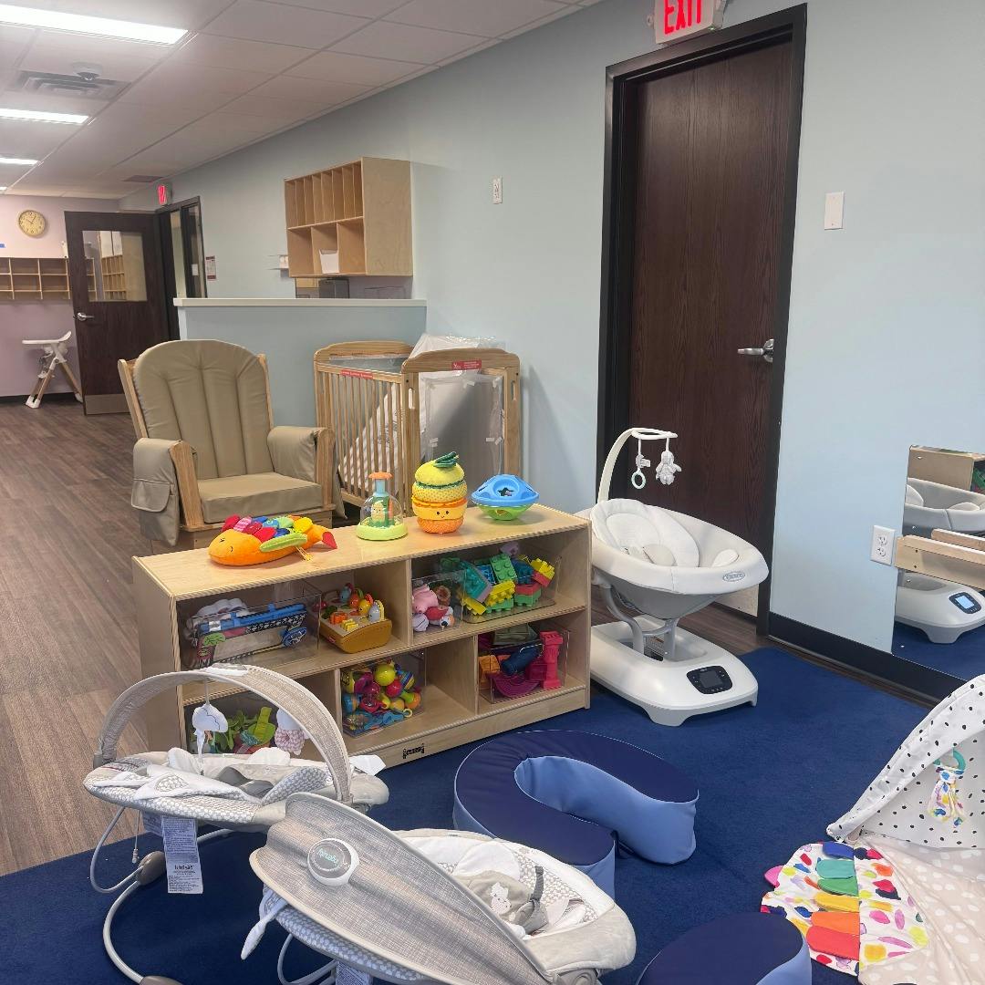Classroom with cribs, chairs, toy shelf, and baby rockers