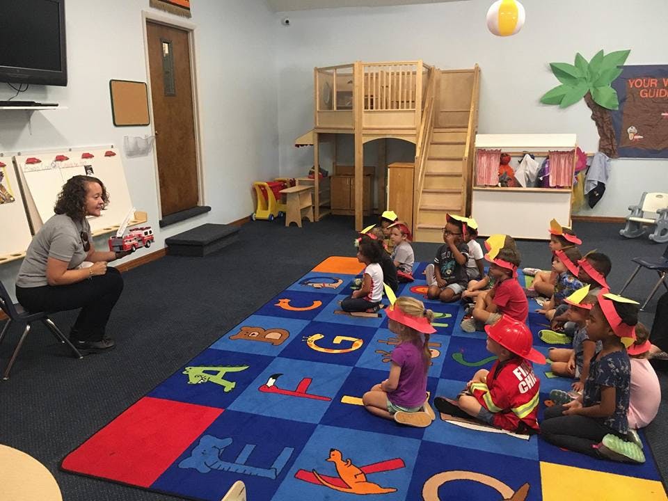 Person reading to a group of children sitting on a rug in a classroom