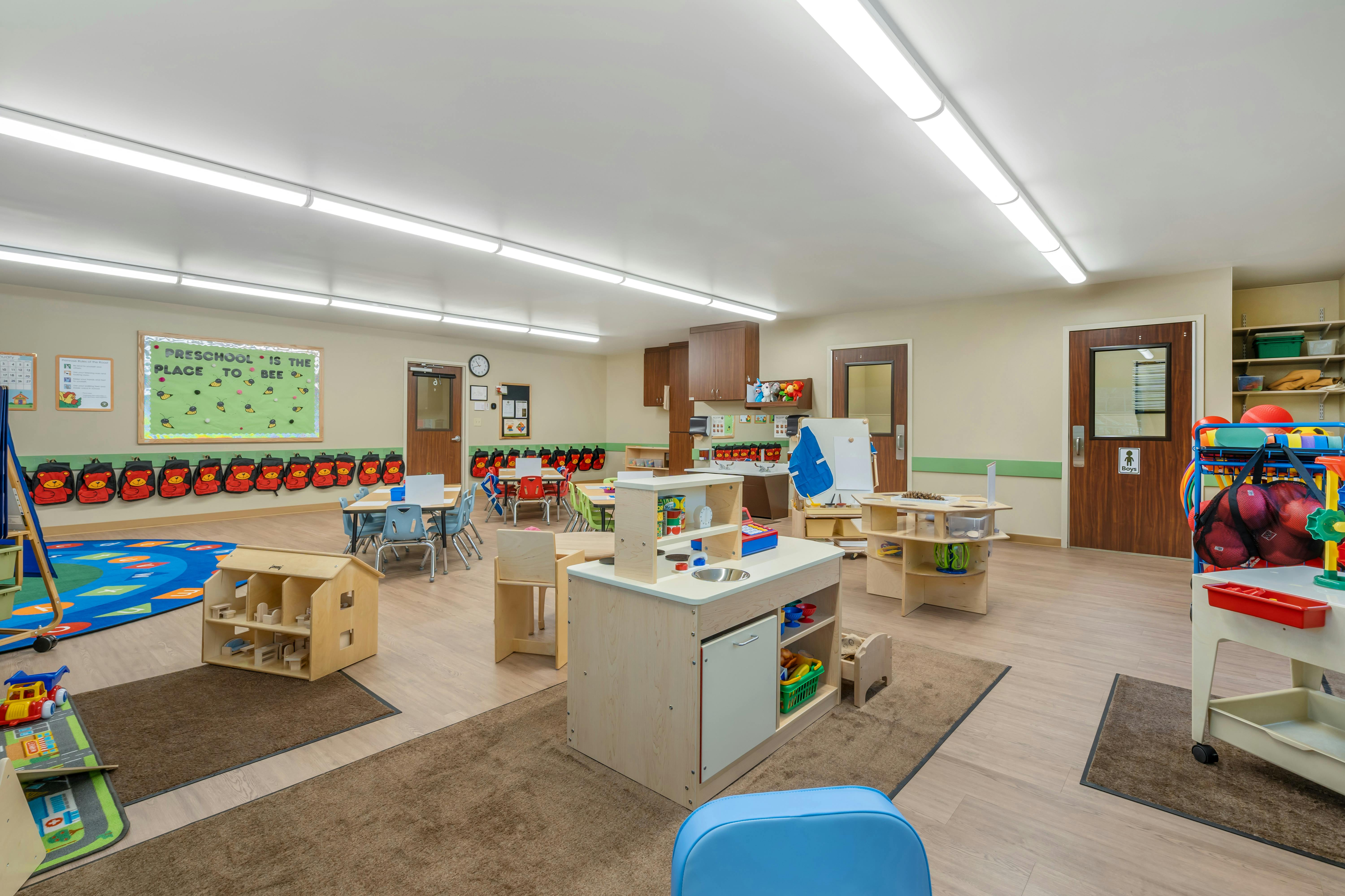 A brightly lit classroom for young children with play areas and small tables