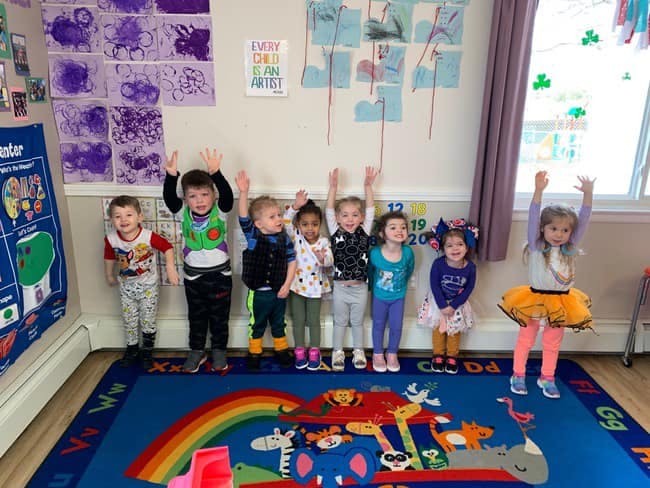 Group of children standing with arms raised in a classroom