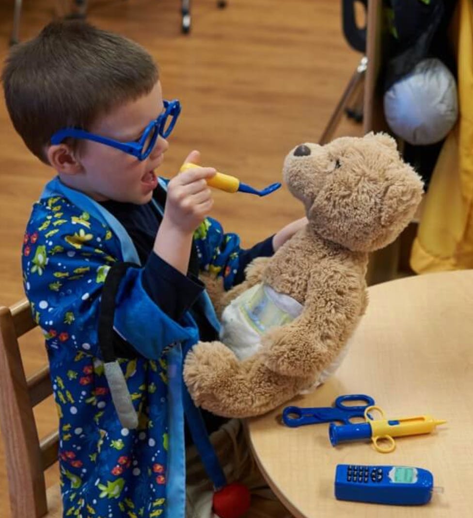 Child in glasses playing with a teddy bear and toy medical tools
