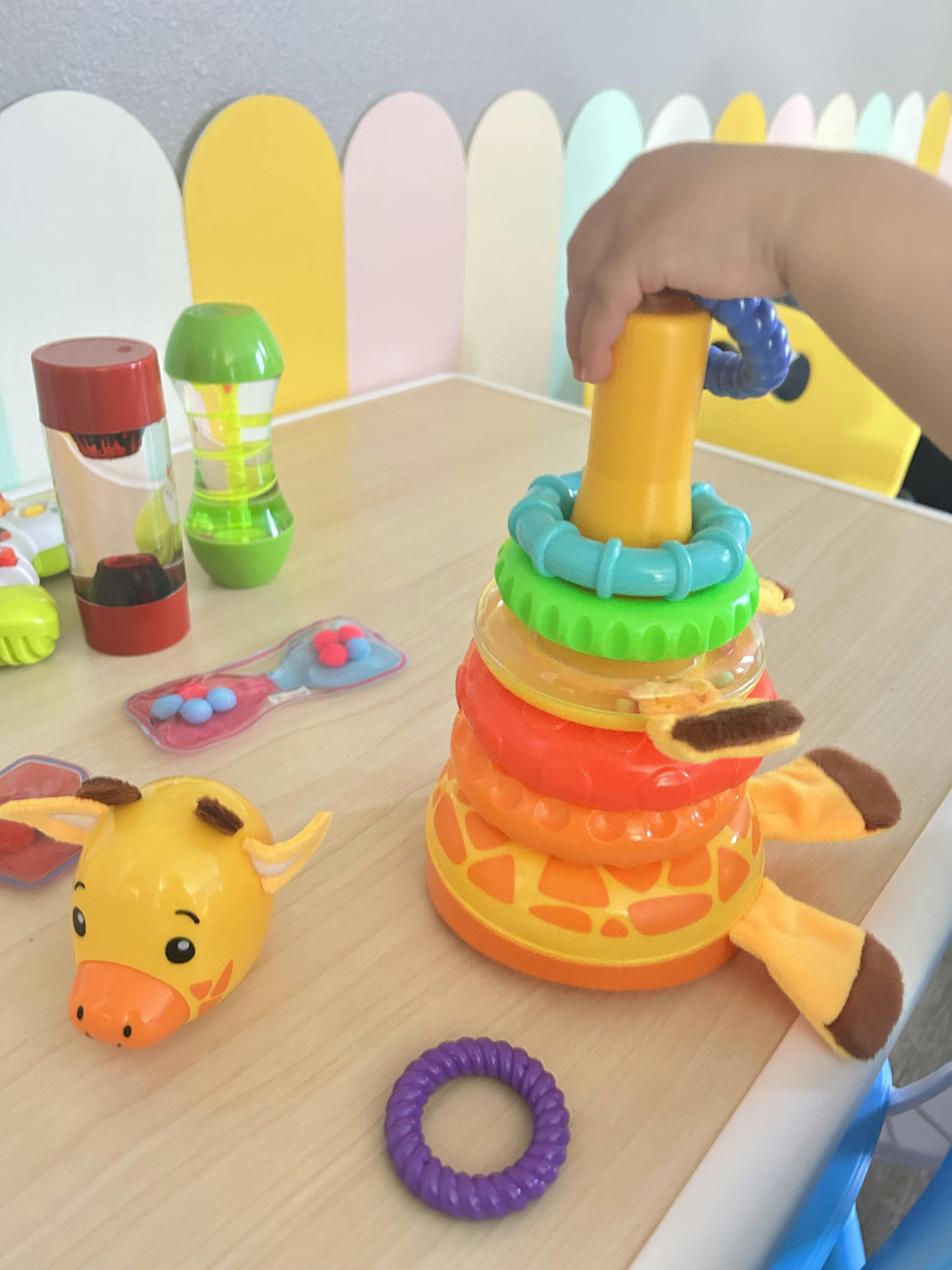 Child hand playing with a giraffe stacking ring toy on a table