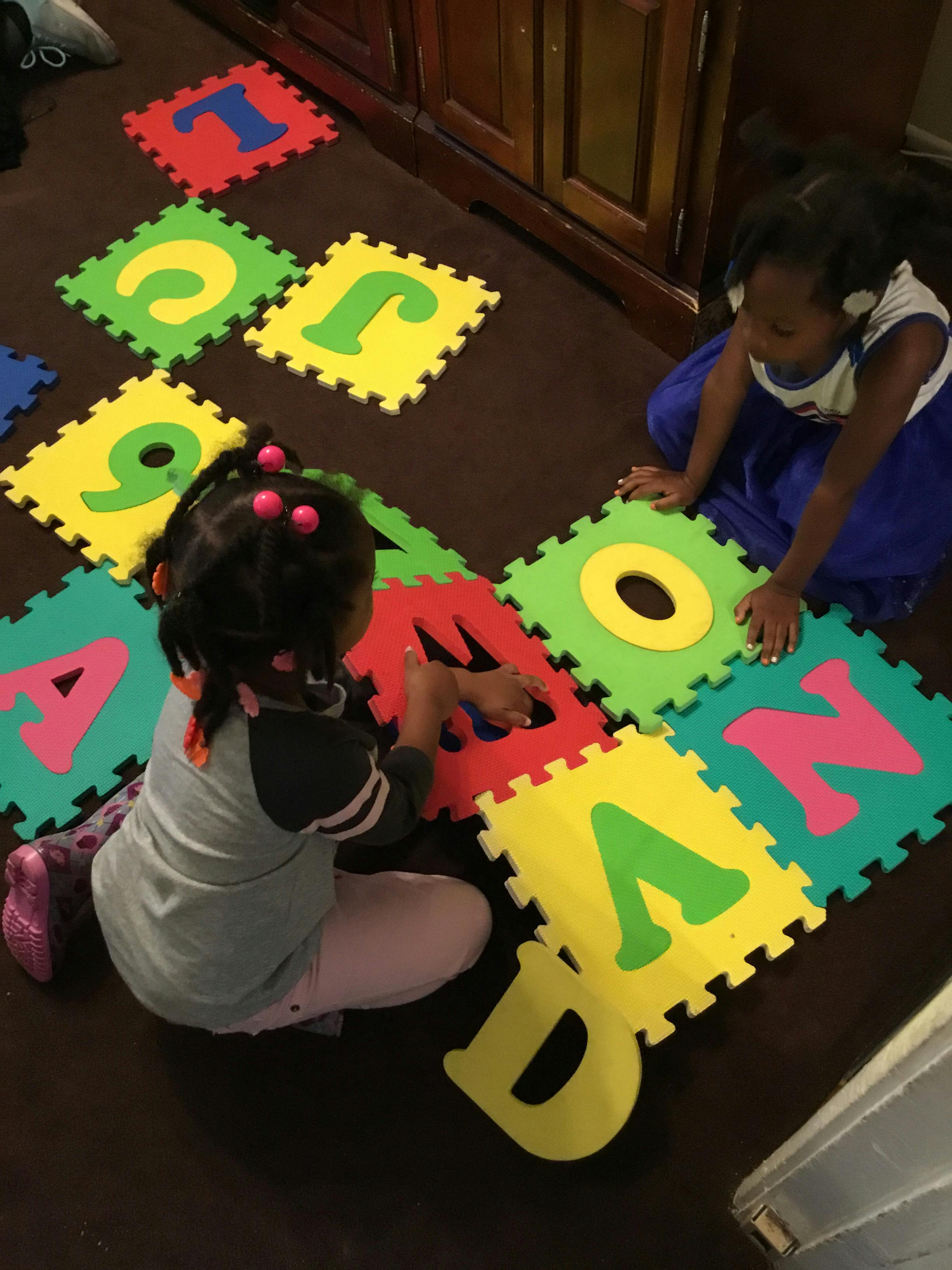 Two children playing with colorful alphabet puzzle mats on the floor