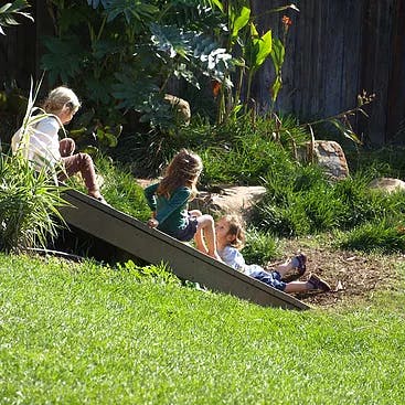 Three children playing on a slide on a grassy hill