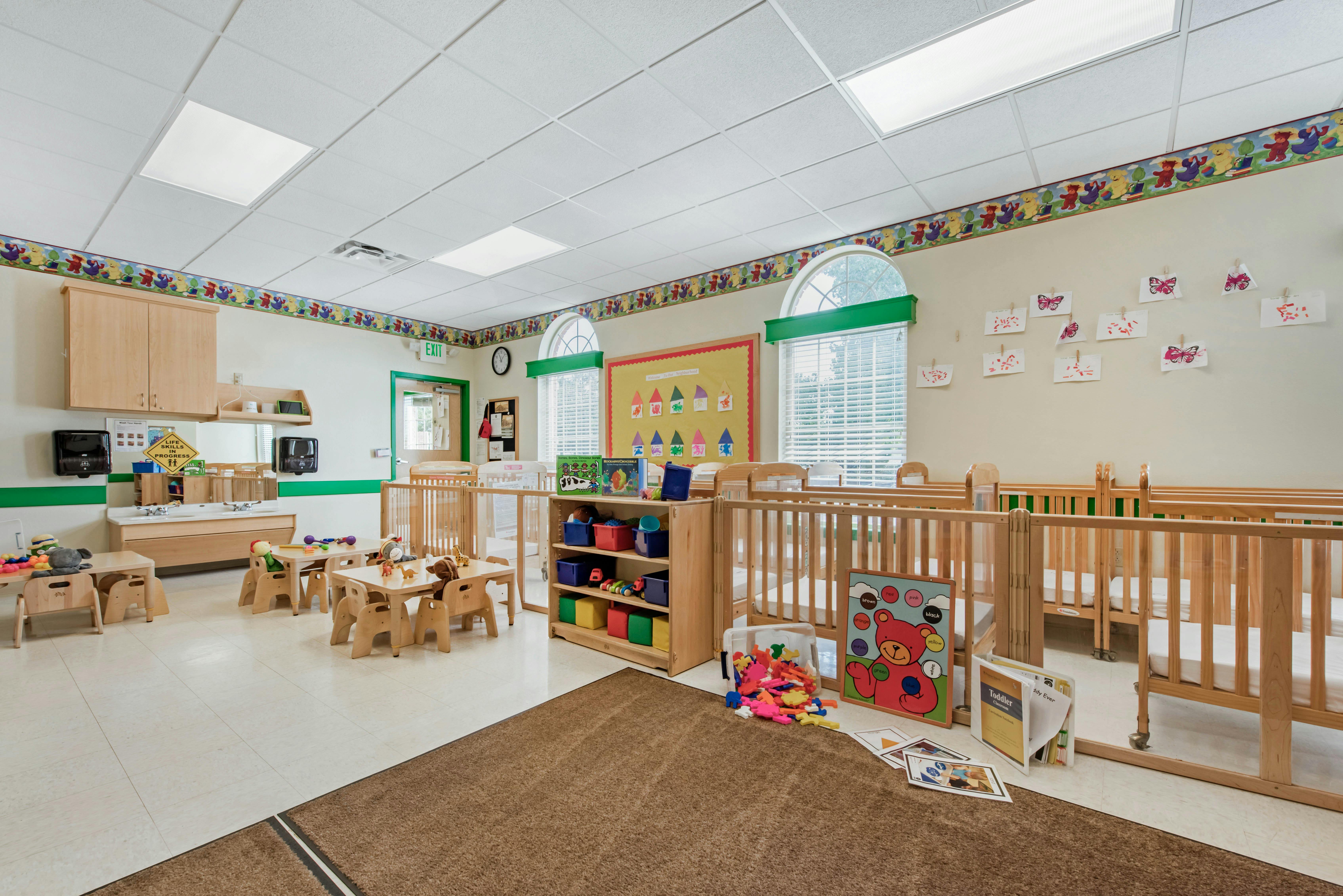Classroom with cribs, small tables and chairs, a sink area, and toys