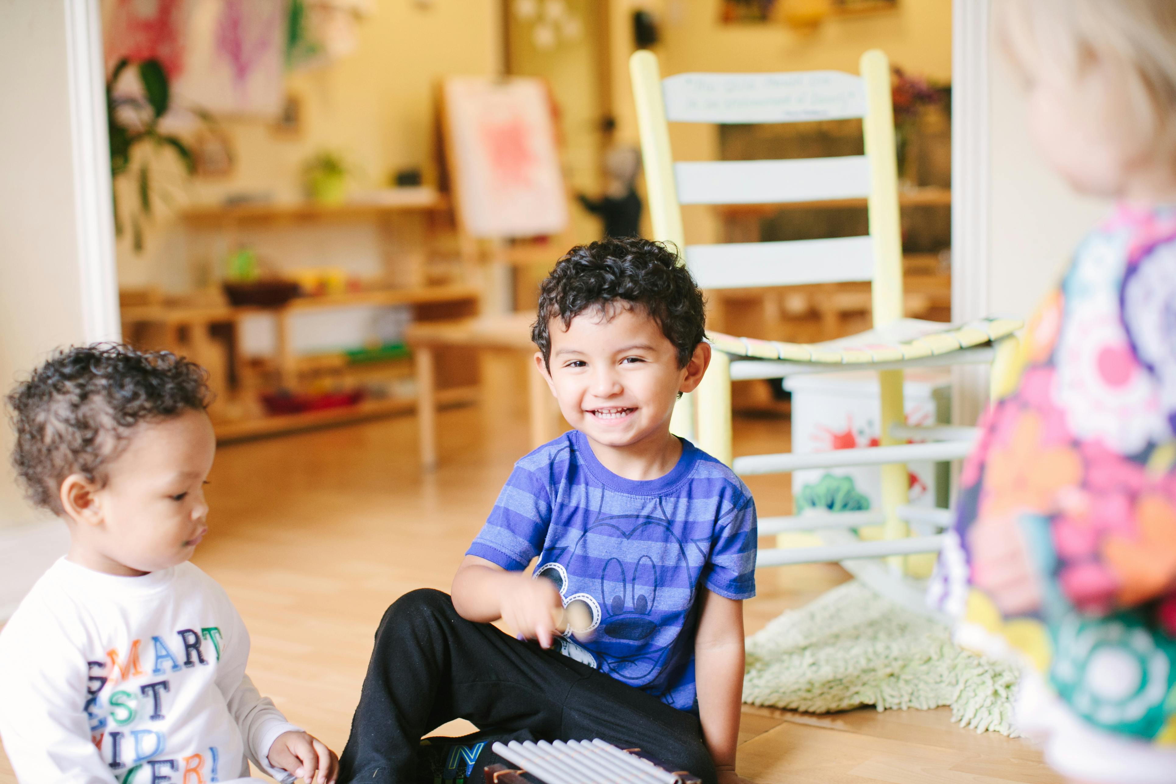 Two children sitting on the floor, one smiling at the camera